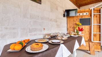 Ein Frühstücksbuffet mit verschiedenen Backwaren und Früchten auf einem Tisch, vor einer rustikalen Steinwand mit Holzbalkendecke.