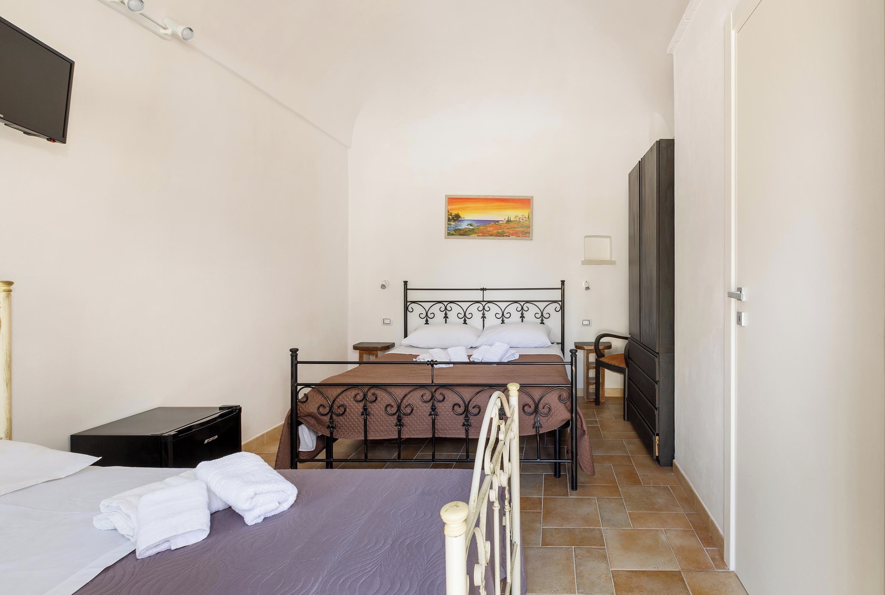 Een slaapkamer met een bed, nachtkastje, stoel, kledingkast en een schilderij aan de muur.