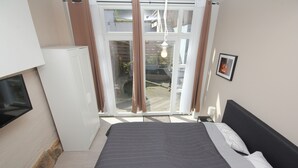 A bedroom with a bed, a television, a sliding glass door, and a small table with a lamp.