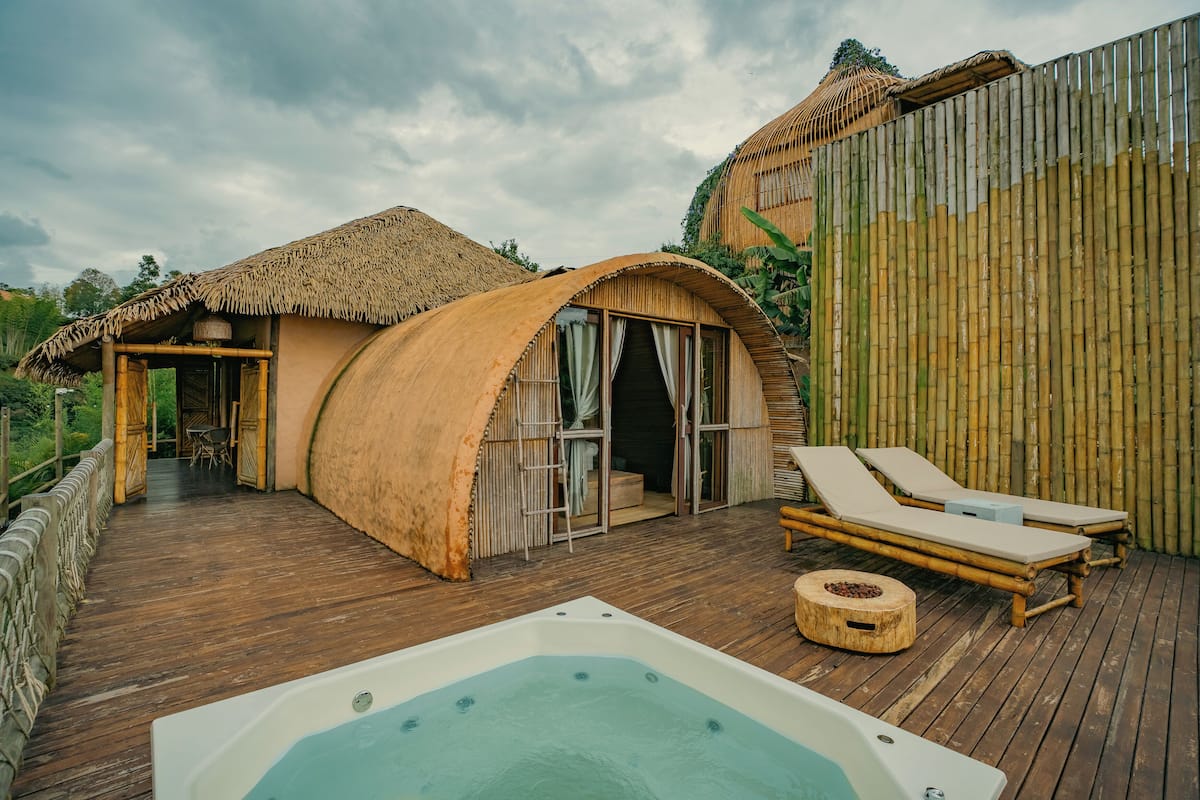 A thatched-roof structure with a wooden deck, a hot tub, and lounge chairs.