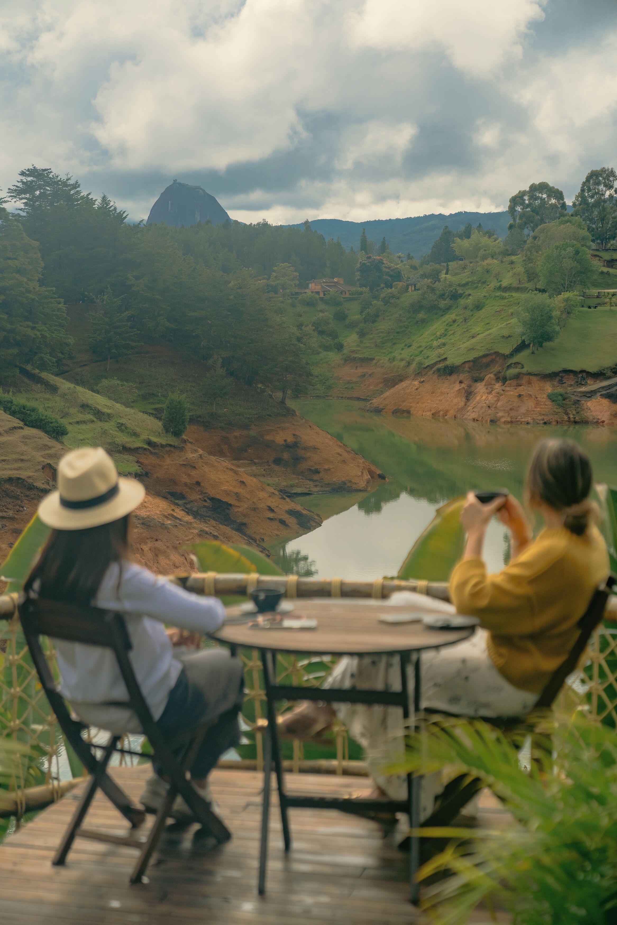 Two people seated at a table with a view of a lake and hills in the background.