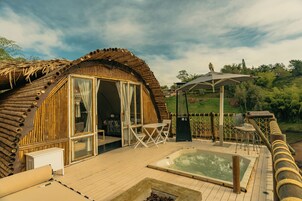 Una estructura de madera con forma de cúpula, con puerta y ventanas de vidrio, un jacuzzi y asientos exteriores.