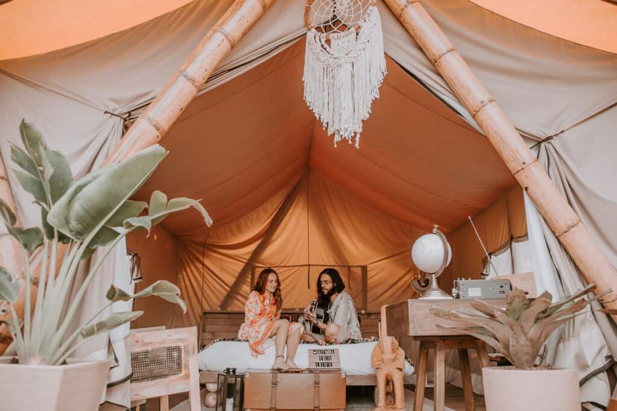 A tent with two people sitting on a bed, surrounded by plants and a globe on a table.