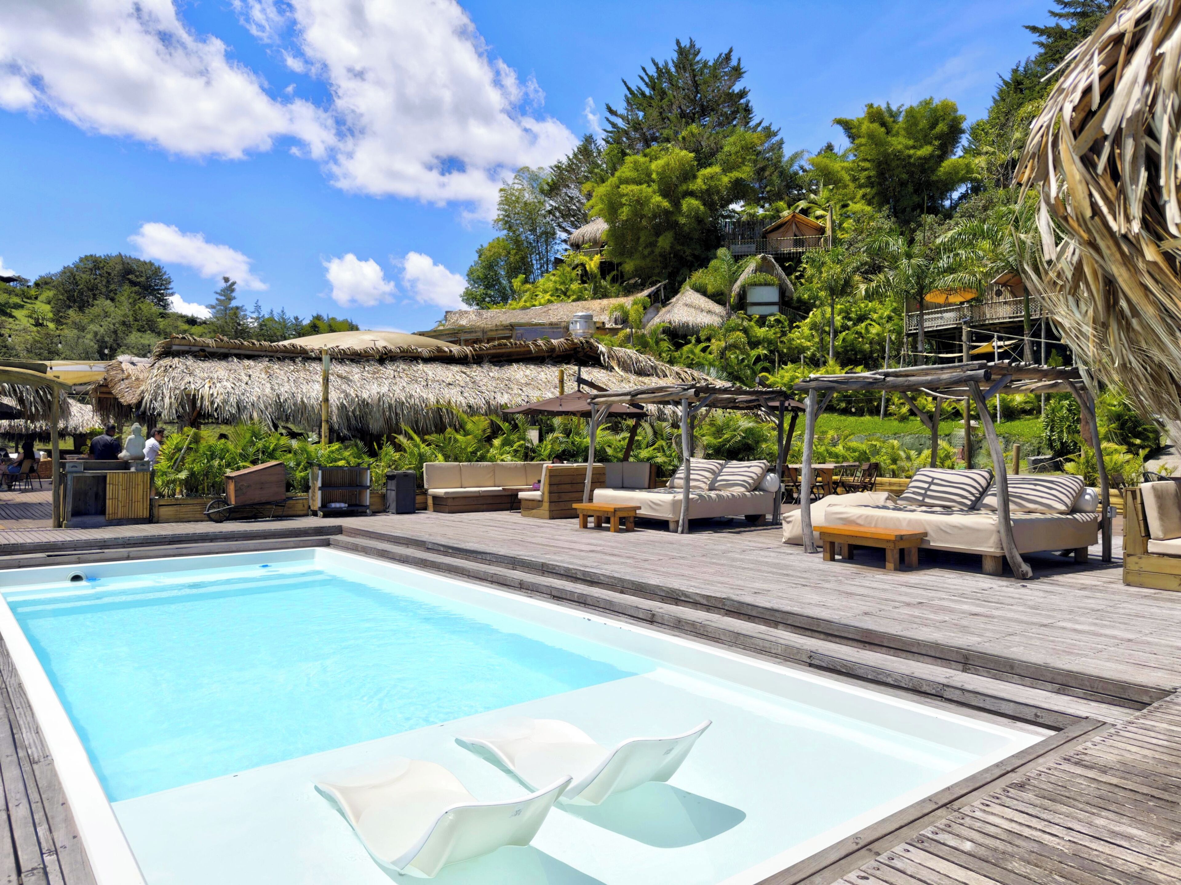 A pool area with lounge chairs and a thatched-roof structure.