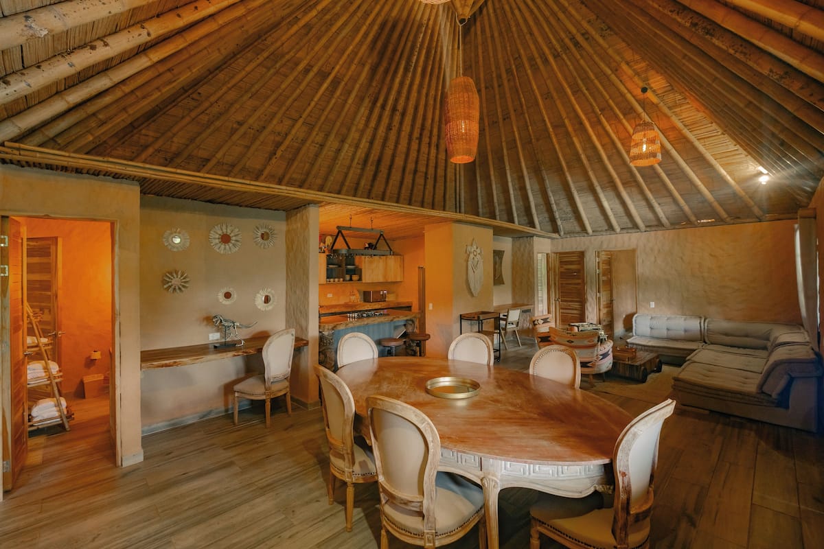 A spacious dining area with a wooden table and chairs, a kitchen in the background, and a high, sloped ceiling.