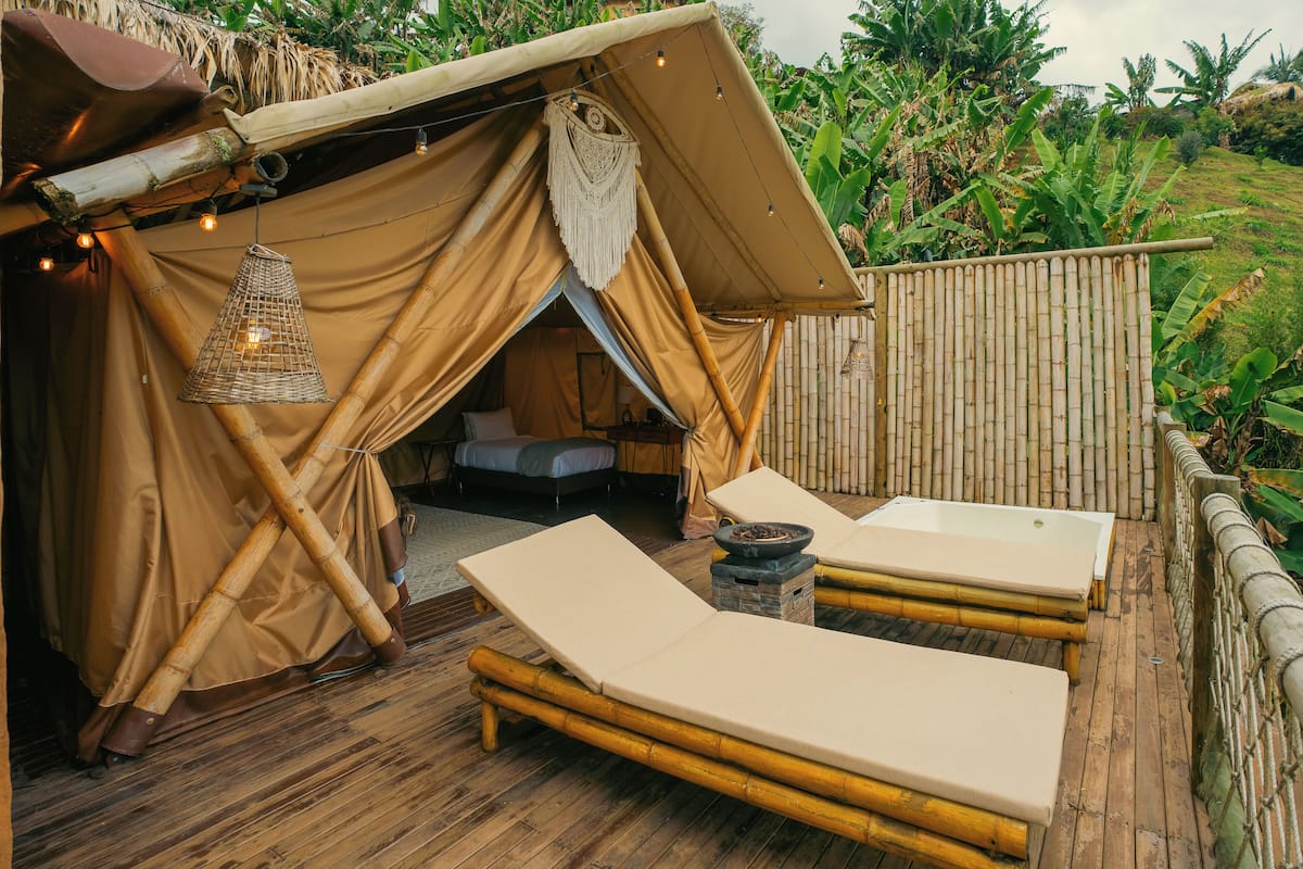 A bamboo-framed tent with a thatched roof, two lounge chairs, and a hanging light fixture.