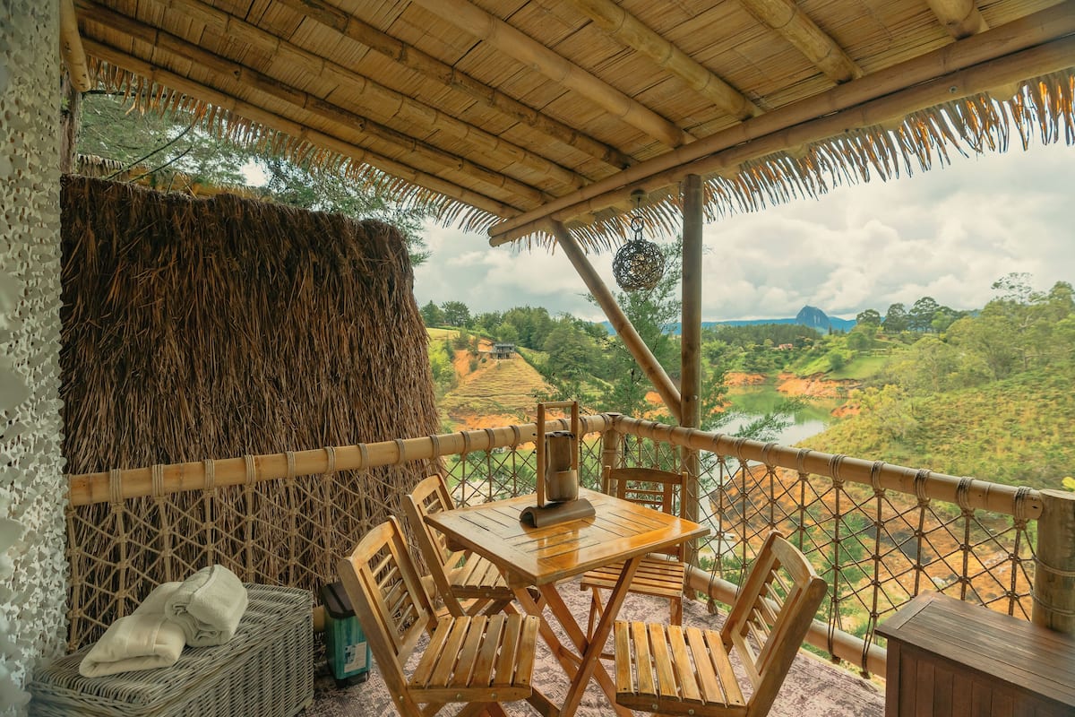A wooden table and chairs set up on a balcony with a view of a river and hills.