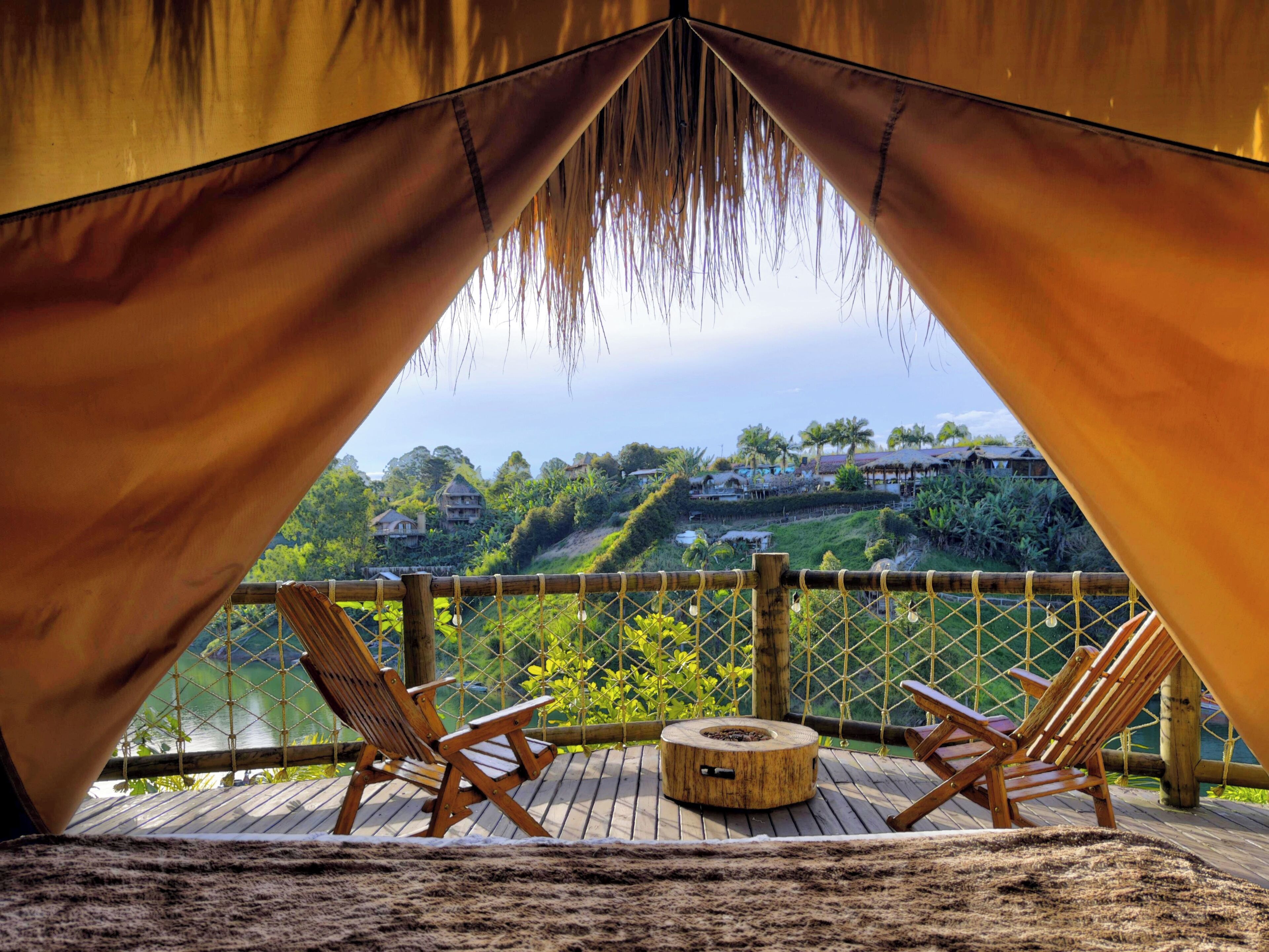 A wooden deck with two wooden chairs and a circular wooden table, overlooking a hillside with buildings and greenery.