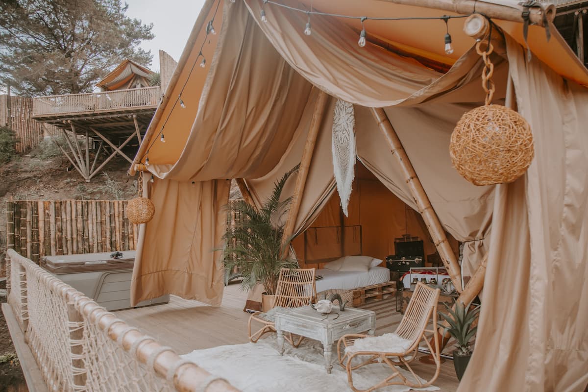A cozy tented accommodation with a balcony, wicker furniture, and a small table.