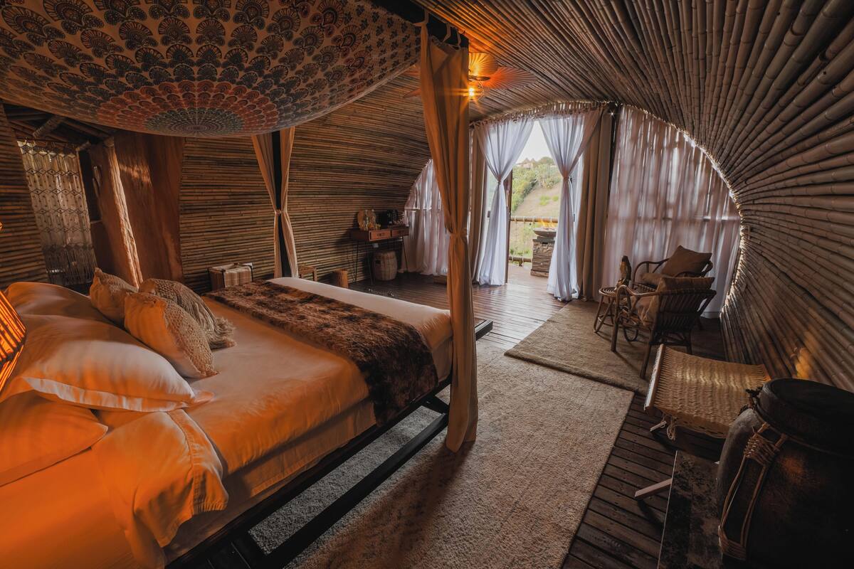A spacious, well-lit room with a large bed, a wooden floor, and a view of the outdoors.