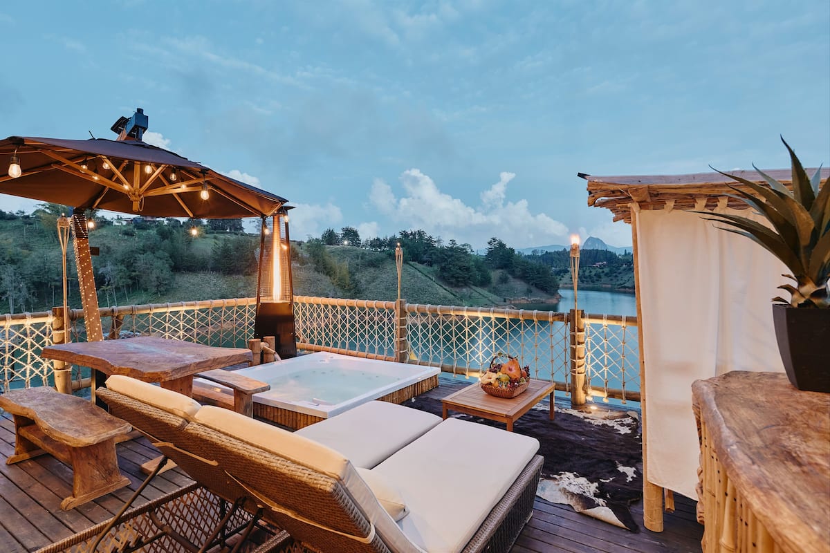 An outdoor deck with wooden furniture, a hot tub, and a view of a lake and mountains.