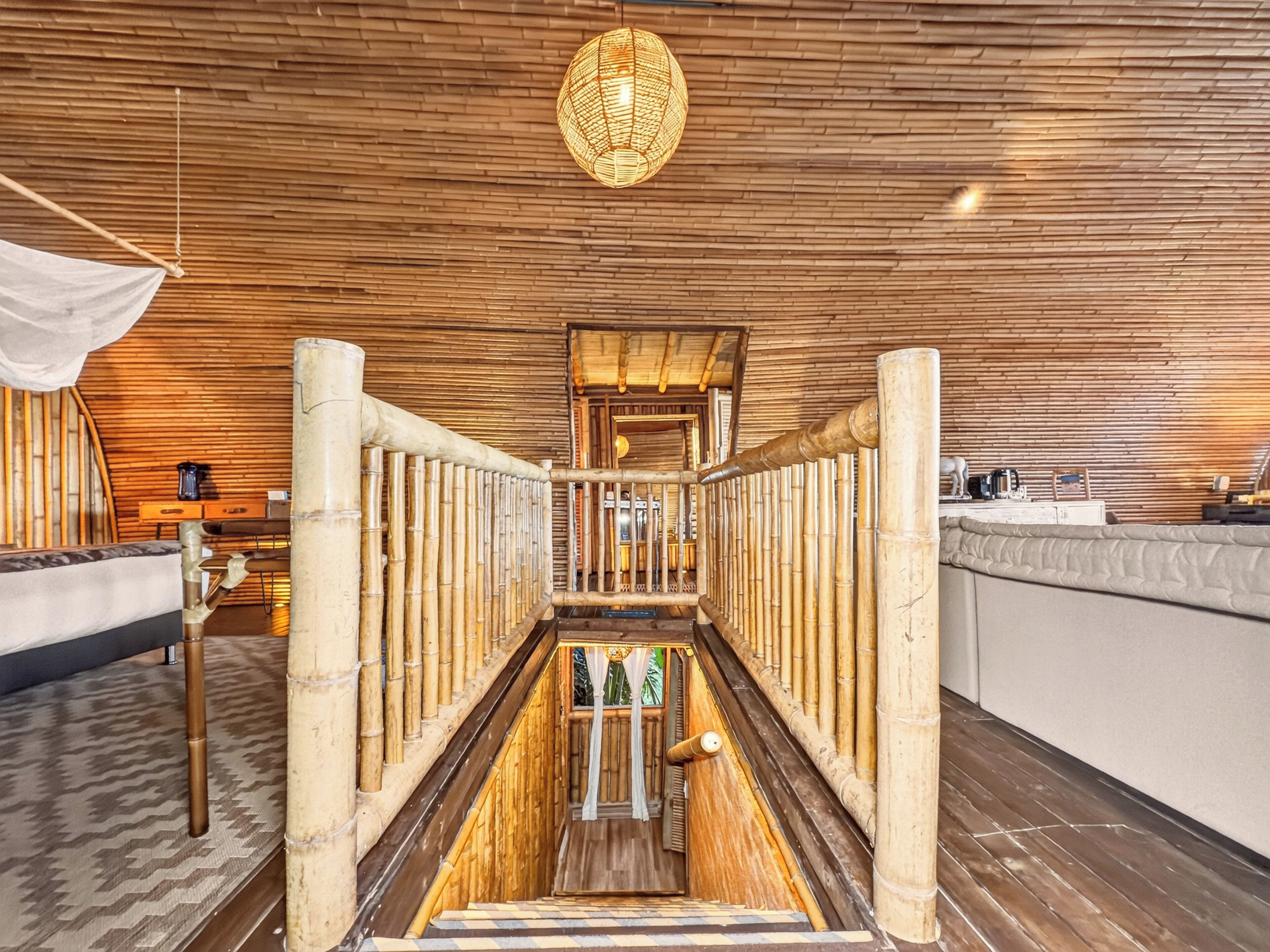 A bamboo-walled room with a central staircase, a hanging light fixture, and a bed with a patterned bedspread.