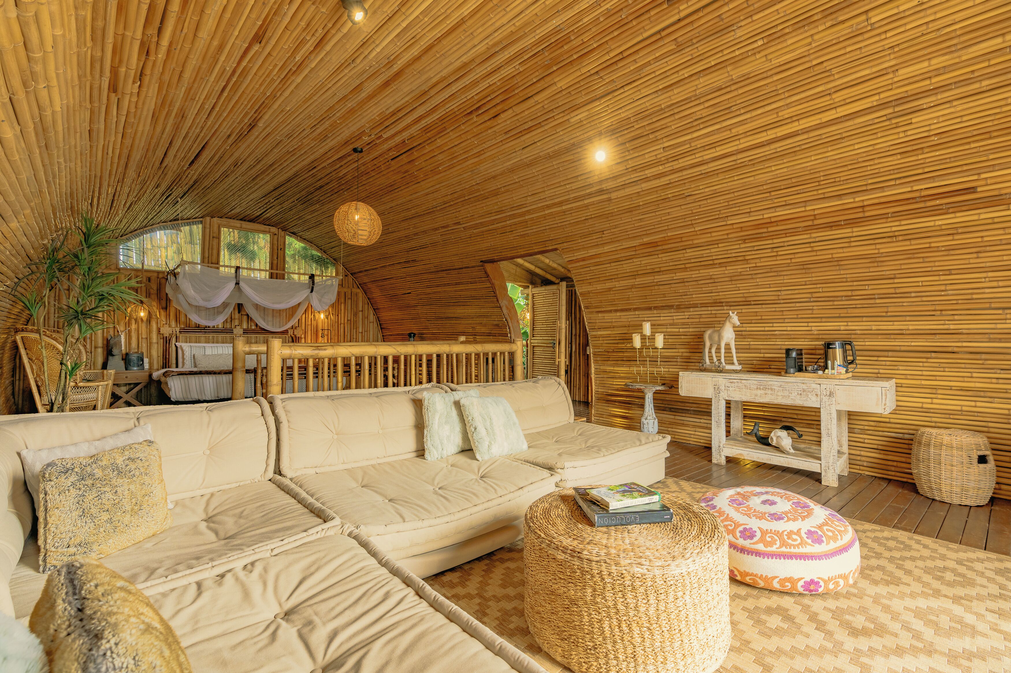 Una sala de estar acogedora, con suelo de madera, un sofá, un reposapiés y una mesita con adornos.