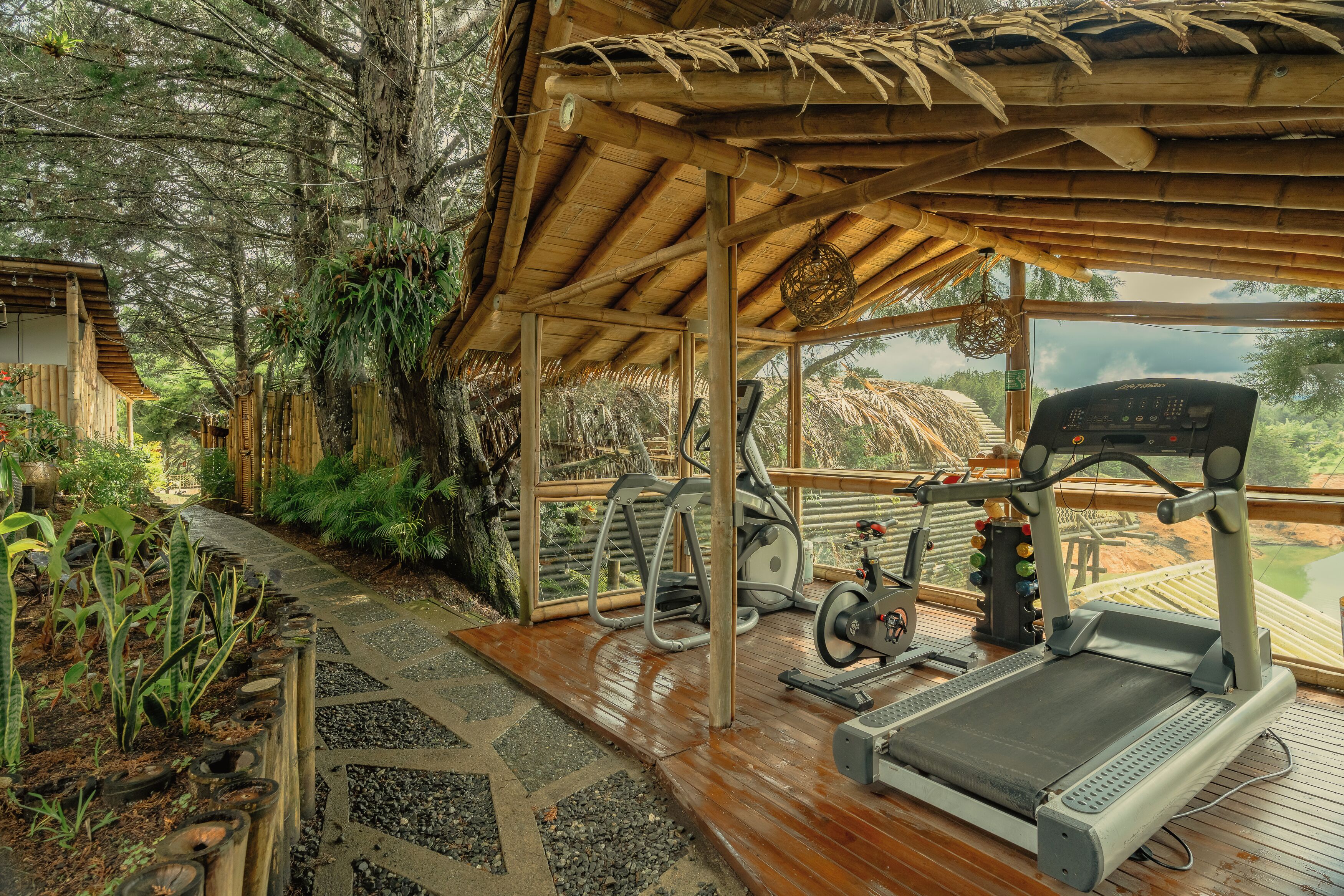 A covered outdoor gym area with exercise equipment, surrounded by tropical vegetation and a wooden deck.