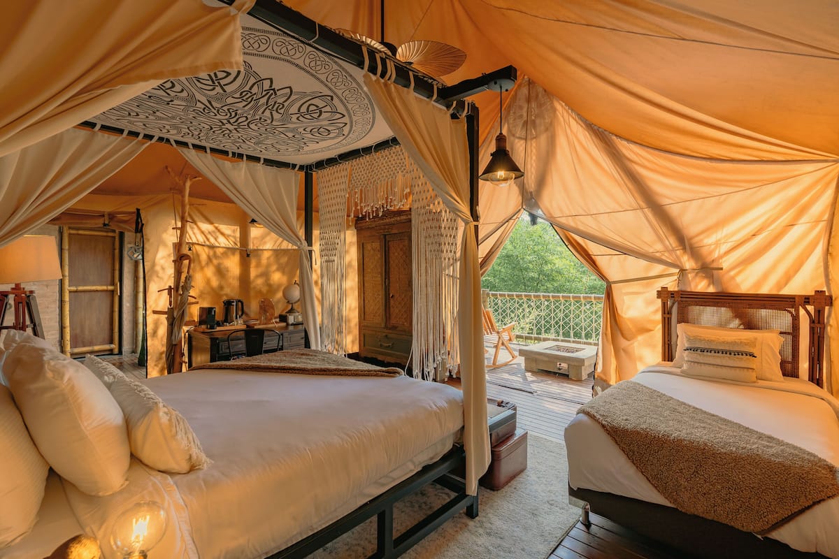 A tented accommodation with a large bed, a smaller bed, and a seating area with a view.