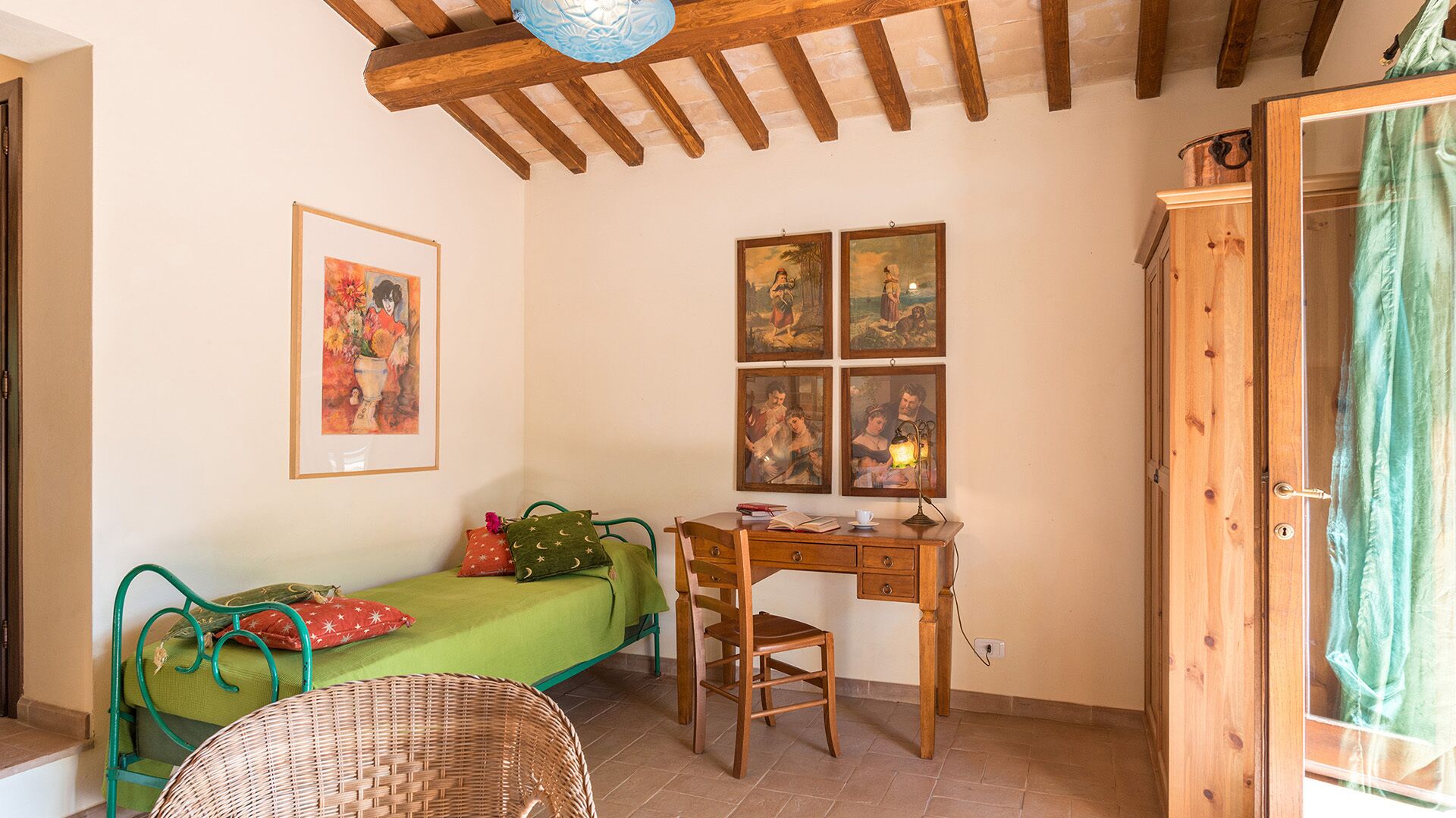 Een gezellige kamer met een houten bureau, een groen bed en een rieten stoel.