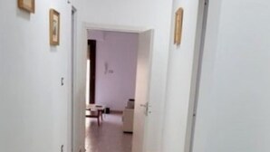 A narrow hallway with a tiled floor leading to a room with a bed and a small table.