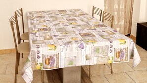 A dining table with a floral tablecloth, surrounded by four chairs, in a room with a clock on the wall and a curtain on the window.