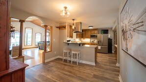 A spacious kitchen with wooden cabinets, a central island with stools, and a large window providing natural light. - NEW: Kids Lifted PlayHouse! Pool, Hot Tub, SportCourt. Minutes From South Haven. (Bangor)