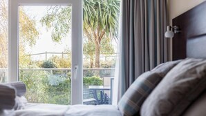 Habitación de hotel con una cama, vistas a un balcón con mesa y sillas, y una palmera.