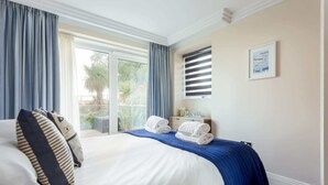 Una habitación de hotel con una cama grande, una mesita de noche con lámpara, una ventana con cortinas y vistas a zonas verdes.