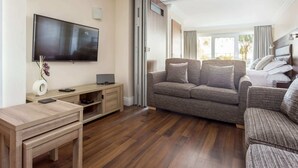 Una sala de estar moderna con un televisor de pantalla plana, una mesa de centro de madera y un sofá gris con varios cojines.