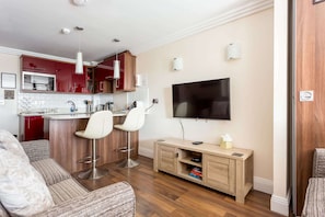 Una sala moderna con un sofá, dos taburetes altos, un televisor y un mueble de madera para entretenimiento.