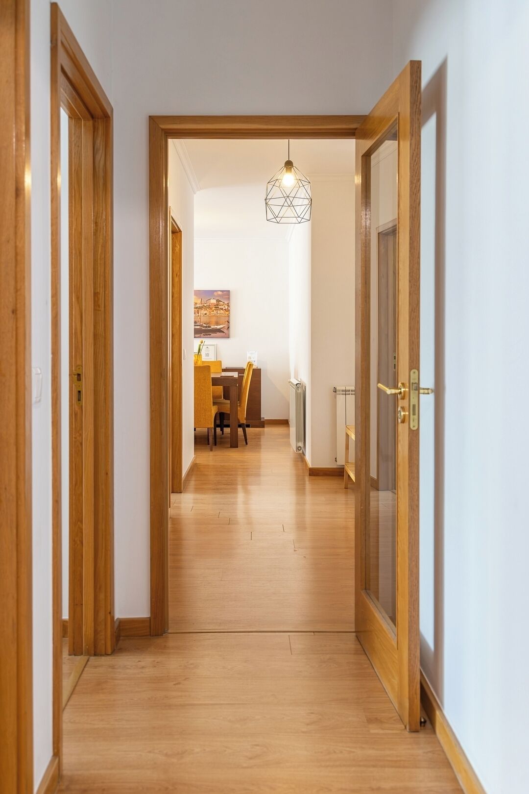A hallway with wooden flooring, a dining area with a table and chairs, and a hanging light fixture.