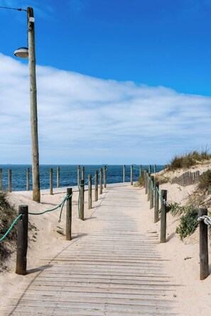 A wooden boardwalk leading to the beach, flanked by wooden posts and ropes.
