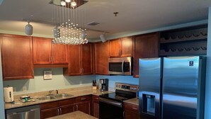 Una cucina moderna con mobili in legno, elettrodomestici in acciaio inossidabile, piani di lavoro in granito e un lampadario originale.