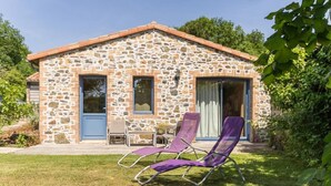 A stone house with a patio, two purple lounge chairs, and a small table. - La Maison des Landes (Gorges)