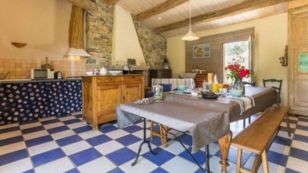A rustic kitchen with a checkered floor, wooden cabinets, and a stone wall. - La Maison des Landes (Gorges)