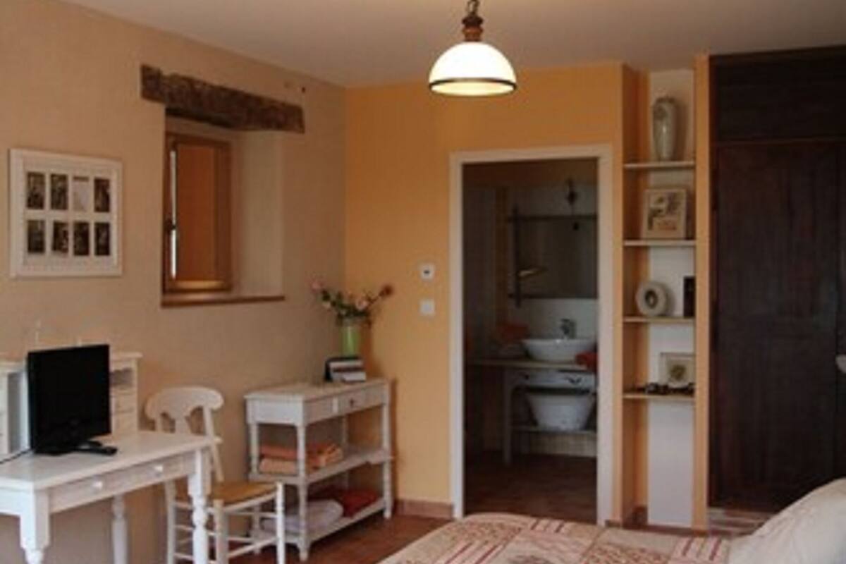 A bedroom with a bed, a desk, a chair, a television, and a bathroom visible through an open door.