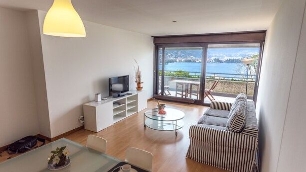 Uma sala de estar moderna com sofá, mesa de centro de vidro, TV e vista para um lago.