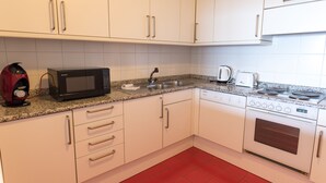 Uma cozinha com armários brancos, micro-ondas, pia, chaleira e fogão.