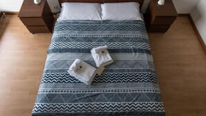 Cama bem arrumada com colcha estampada, dois travesseiros e duas mesas de cabeceira com luminárias.