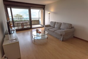 A modern living room with a glass coffee table, striped sofa, and a view of a balcony with a table and chairs. - Paradise (Paradiso)