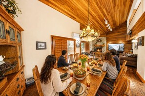 Un comedor con mesa de madera, sillas, una araña y chimenea.
