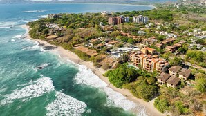 An aerial view of a coastal residential area with beachfront properties, dense vegetation, and a distant mountain range.