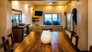 A dining area with a wooden table, a vase, and a view of the ocean through large windows.