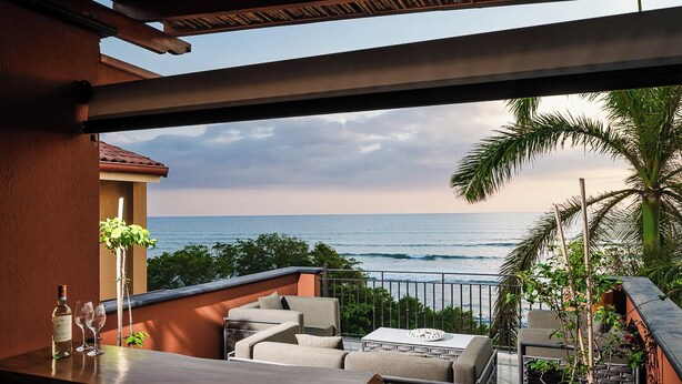 A balcony with outdoor seating, a view of the ocean, and a potted plant.