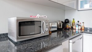 Een keuken met een magnetron, broodrooster, waterkoker en diverse keukenbenodigdheden op het aanrecht.