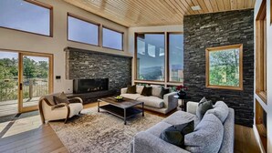 Una sala de estar moderna con chimenea de piedra, ventanas amplias y techo de madera.