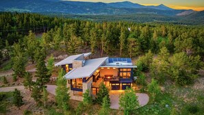 Una casa moderna con una amplia terraza, rodeada de un bosque denso y montañas.