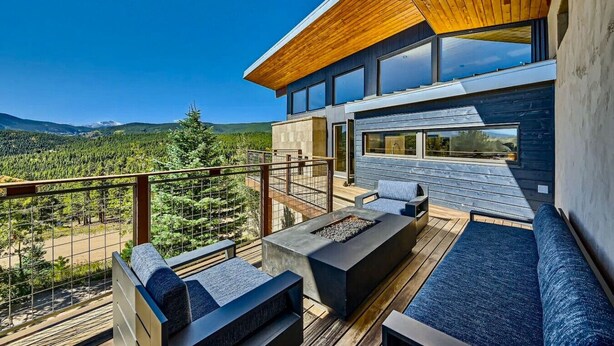 Una terraza moderna al aire libre con una chimenea, asientos y vistas a un paisaje boscoso.