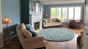 A living room with a beige sofa, a blue rug, a fireplace, and a large window with a view of trees.