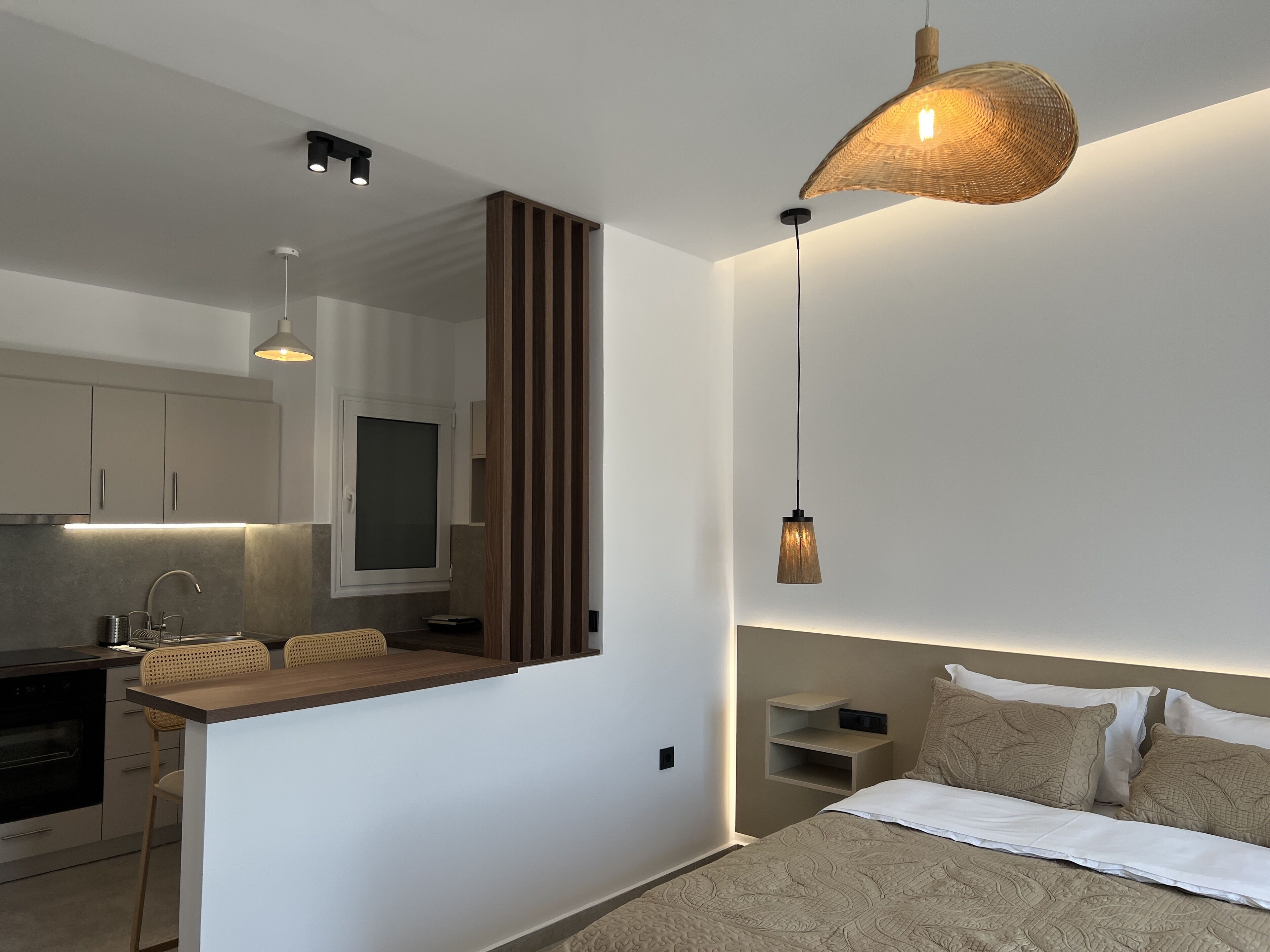 Un dormitorio moderno con una cama grande, mesitas de noche y una mesilla. Cuenta con una zona de cocina con encimera y lavabo.