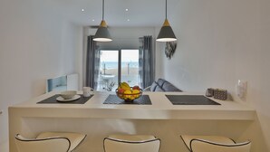 Un espace de salle à manger moderne avec un îlot central, deux suspensions et une vue sur l’extérieur grâce à de grandes fenêtres.