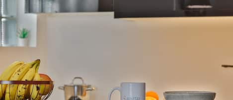 A kitchen counter with a fruit bowl containing bananas and an apple, a white mug with the text "SAIRSTAY," and a gray bowl on a matching saucer.