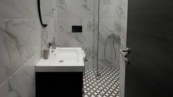 Ein modernes Badezimmer mit Marmorwand, einem schwarzen Schrank, einem weißen Waschbecken und einem geometrisch gemusterten Boden.